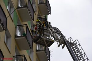 Strażak w koszu podnośnika przy balkonie jednego z mieszkań bloku